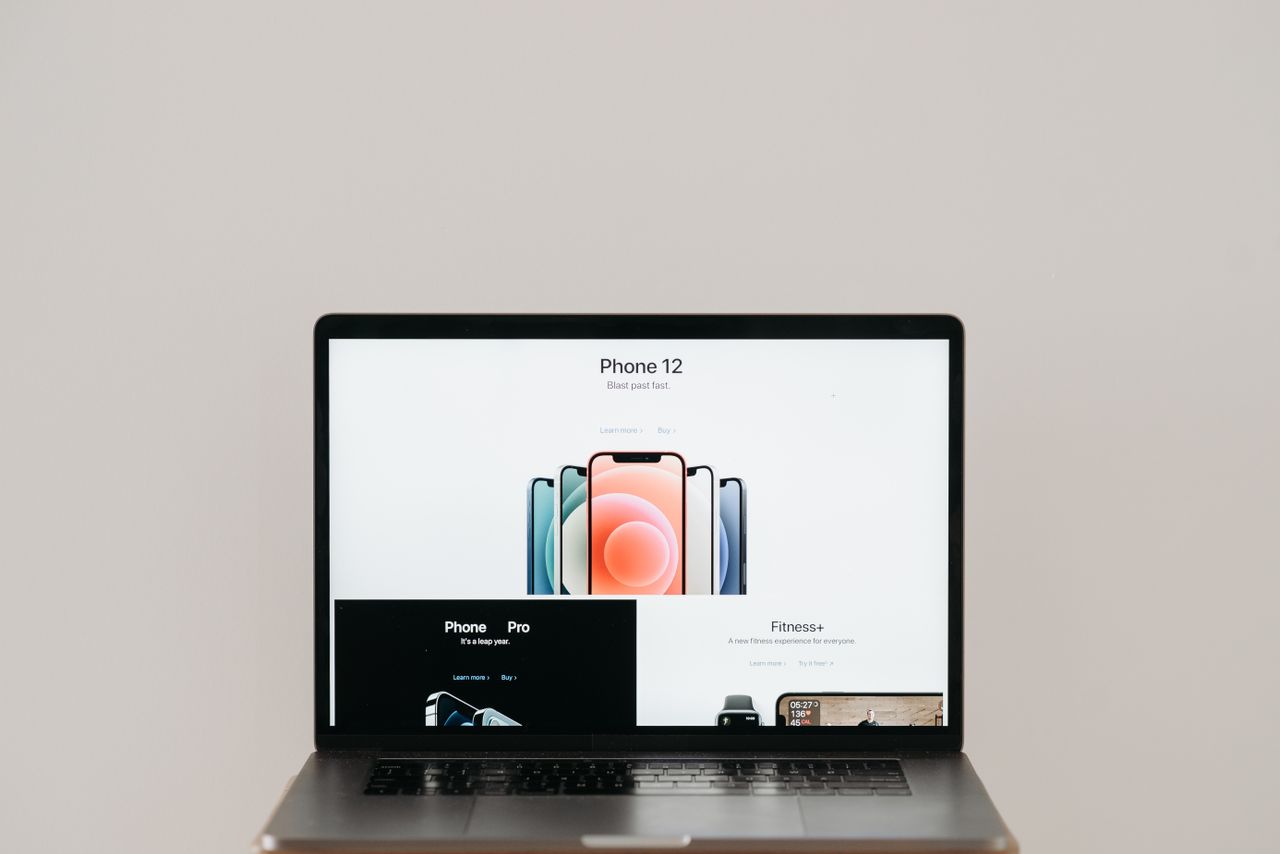 home-hero-bg Laptop on stool showing sleek iPhone 12 ad, white background.